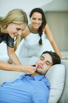 Frau trägt Lippenstift auf schlafenden Mann auf - CAIF04598