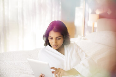 Woman in bathrobe using digital tablet on bed - HOXF00224