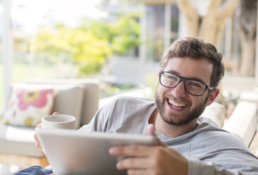 Porträt eines lächelnden Mannes, der Kaffee trinkt und ein digitales Tablet benutzt - HOXF00230