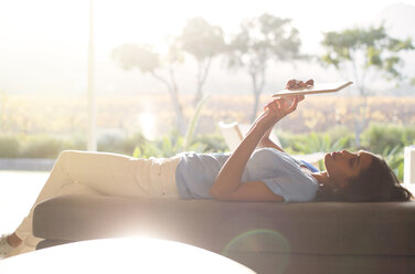 Woman laying on chaise lounge using digital tablet on sunny patio - HOXF00240