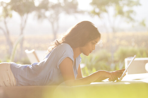 Woman laying using digital tablet on sunny patio - HOXF00245