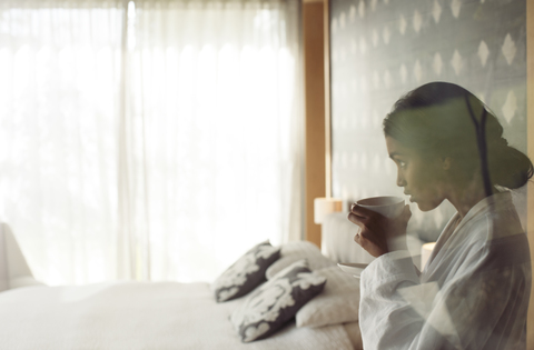 Frau im Bademantel schlürft Kaffee im Schlafzimmer, lizenzfreies Stockfoto