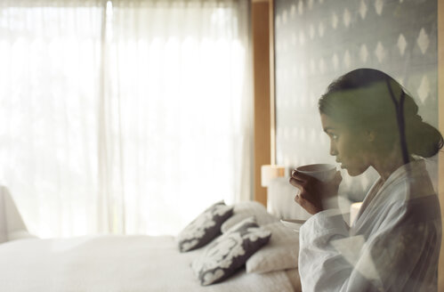 Frau im Bademantel schlürft Kaffee im Schlafzimmer - HOXF00262