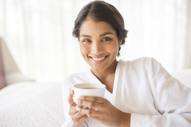 Portrait smiling woman in bathrobe drinking tea - HOXF00276