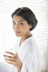 Portrait confident woman in bathrobe drinking water - HOXF00285