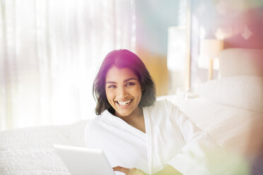 Portrait smiling woman in bathrobe using digital tablet on bed - HOXF00292