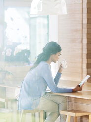 Woman drinking coffee and using digital tablet at breakfast bar - HOXF00299