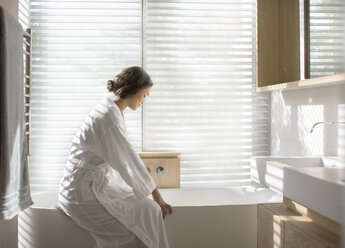 Woman in bathrobe drawing a bath in soaking tub in luxury bathroom - HOXF00306