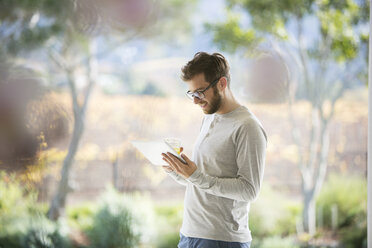 Man drinking orange juice and using digital tablet on patio - HOXF00310