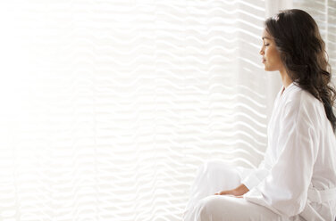 Gelassene Frau im Bademantel meditiert am sonnigen Fenster - HOXF00311