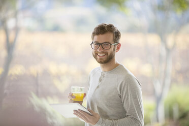 Porträt eines lächelnden Mannes, der auf einer Terrasse Orangensaft trinkt und ein digitales Tablet benutzt - HOXF00312