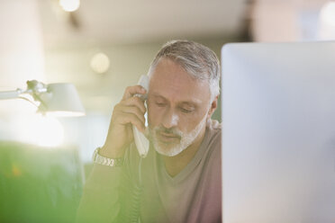 Businessman talking on telephone at computer in office - HOXF00356