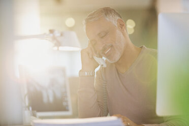 Businessman talking on telephone in sunny office - HOXF00366