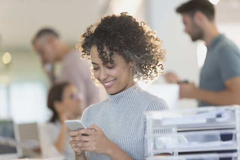 Lächelnde Geschäftsfrau, die mit ihrem Handy im Büro SMS schreibt - HOXF00383