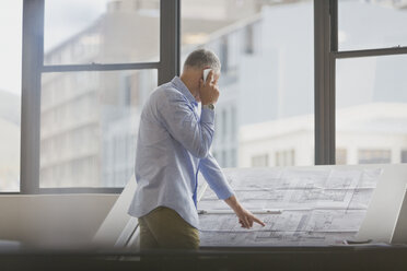 Architekt, der mit seinem Handy telefoniert und Baupläne im Büro überprüft - HOXF00384