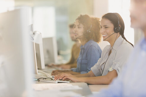 Lächelnde Geschäftsfrau mit Headset bei der Arbeit am Computer im Büro - HOXF00389