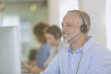 Businessman with headset working at computer in office - HOXF00400