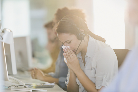Geschäftsfrau mit Headset schnäuzt sich am Computer bei der Arbeit, lizenzfreies Stockfoto
