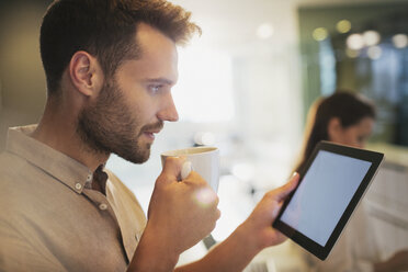 Businessman drinking coffee using digital tablet in office - HOXF00402
