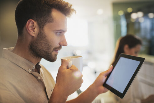 Geschäftsmann trinkt Kaffee mit digitalem Tablet im Büro - HOXF00402