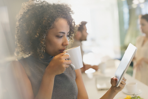 Geschäftsfrau trinkt Kaffee und benutzt ein digitales Tablet, lizenzfreies Stockfoto