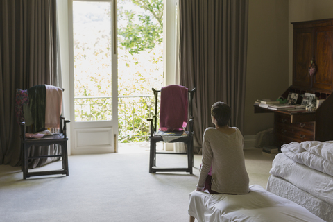 Frau blickt aus dem Balkonfenster in einem luxuriösen Musterschlafzimmer, lizenzfreies Stockfoto