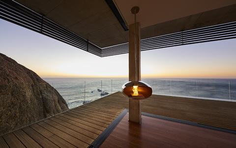 Moderner Hängekamin auf der Terrasse eines luxuriösen Strandhauses mit Blick auf den Sonnenuntergang am Meer, lizenzfreies Stockfoto