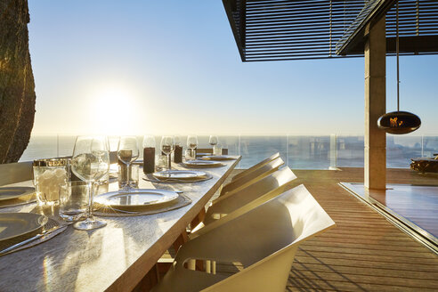 Sun shining over ocean behind luxury patio dining table with placesettings - HOXF00468