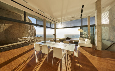Die Sonne scheint in einem modernen, luxuriösen Musterhaus, das ein Esszimmer mit Meerblick bietet - HOXF00481