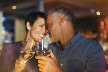 Affectionate couple toasting white wine glasses in bar - HOXF00525