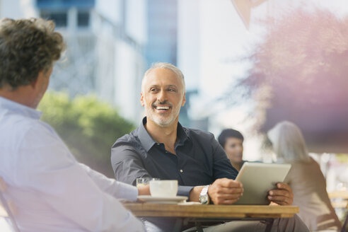 Lächelnde Geschäftsleute, die sich unterhalten, Kaffee trinken und ein digitales Tablet in einem Straßencafé benutzen - HOXF00529