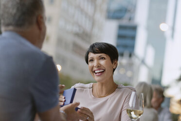 Lächelnde Frau, die ein Geschenk von ihrem Mann in einem Straßencafé erhält - HOXF00545