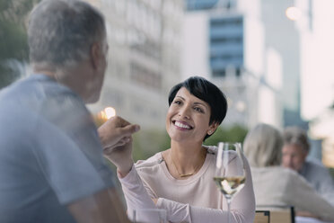 Affectionate couple holding hands and drinking white wine at urban sidewalk cafe - HOXF00546