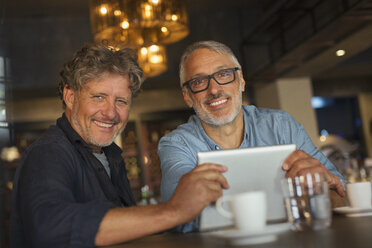 Porträt eines lächelnden Mannes, der ein digitales Tablet benutzt und am Restauranttisch Kaffee trinkt - HOXF00550