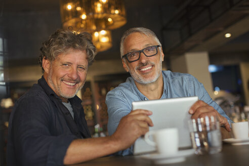 Porträt eines lächelnden Mannes, der ein digitales Tablet benutzt und am Restauranttisch Kaffee trinkt - HOXF00550
