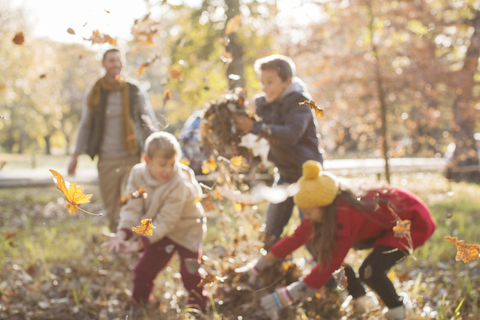 Familie spielt im Herbstlaub im Park, lizenzfreies Stockfoto