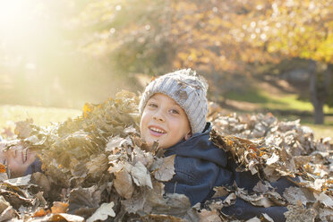 Portrait smiling boys covered in autumn leaves - HOXF00583
