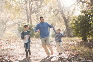 Playful father and sons running on trail in woods - HOXF00585