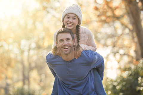 Porträt begeisterter Vater, der seine Tochter im Freien huckepack nimmt, lizenzfreies Stockfoto