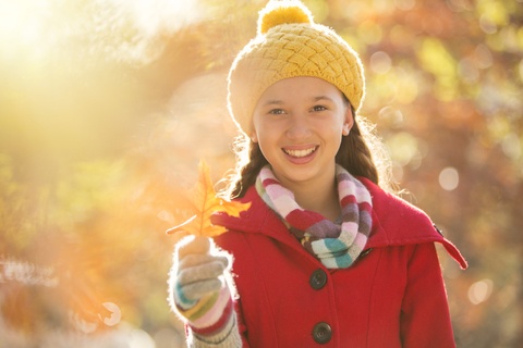 Portrait smiling girl holding golden autumn leaf stock photo
