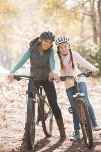 Portrait lächelnde Mutter und Tochter auf Mountainbikes im Wald - HOXF00601