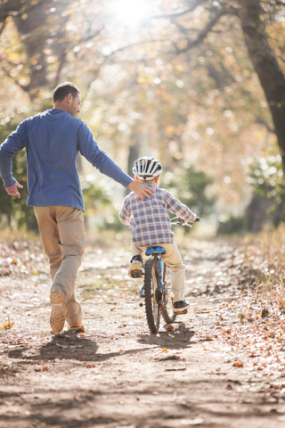 Vater bringt seinem Sohn das Fahrradfahren auf einem Waldweg bei, lizenzfreies Stockfoto