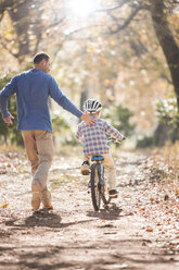 Vater bringt seinem Sohn das Fahrradfahren auf einem Waldweg bei - HOXF00603