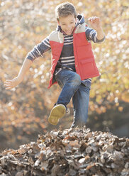 Enthusiastic boy jumping over pile of autumn leaves - HOXF00626