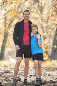 Porträt lächelnder Vater und Sohn in Sportkleidung auf einem Weg im Wald - HOXF00629