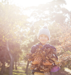Porträt lächelnder Junge, der einen Strauß Herbstblätter hält - HOXF00633