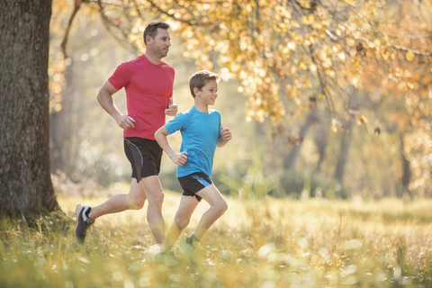 Vater und Sohn joggen im herbstlichen Park, lizenzfreies Stockfoto