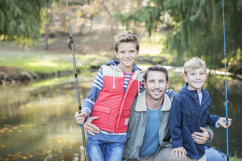 Portrait lächelnder Vater und Söhne mit Angelruten, lizenzfreies Stockfoto