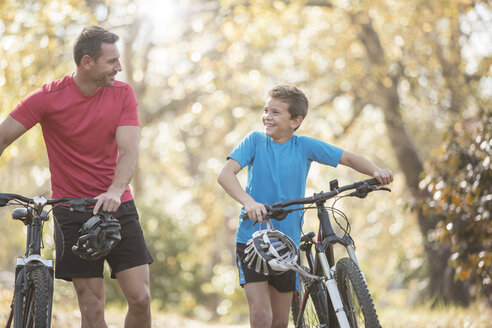 Vater und Sohn zu Fuß mit dem Mountainbike im Wald - HOXF00647