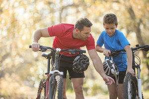 Vater und Sohn untersuchen das Rad eines Mountainbikes - HOXF00652